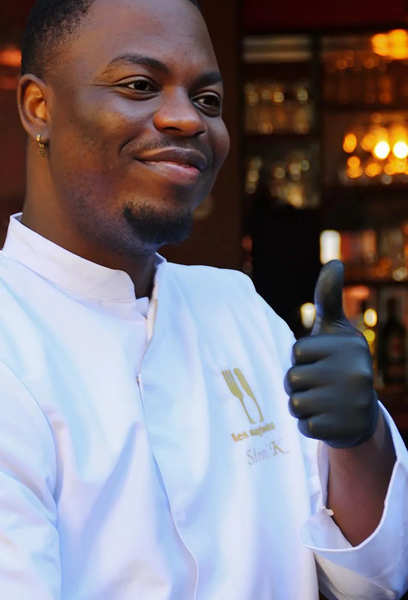 Le chef Stevril, sourire aux lèvres, présentant une assiette devant le bar du restaurant Les Magnolias à Nîmes